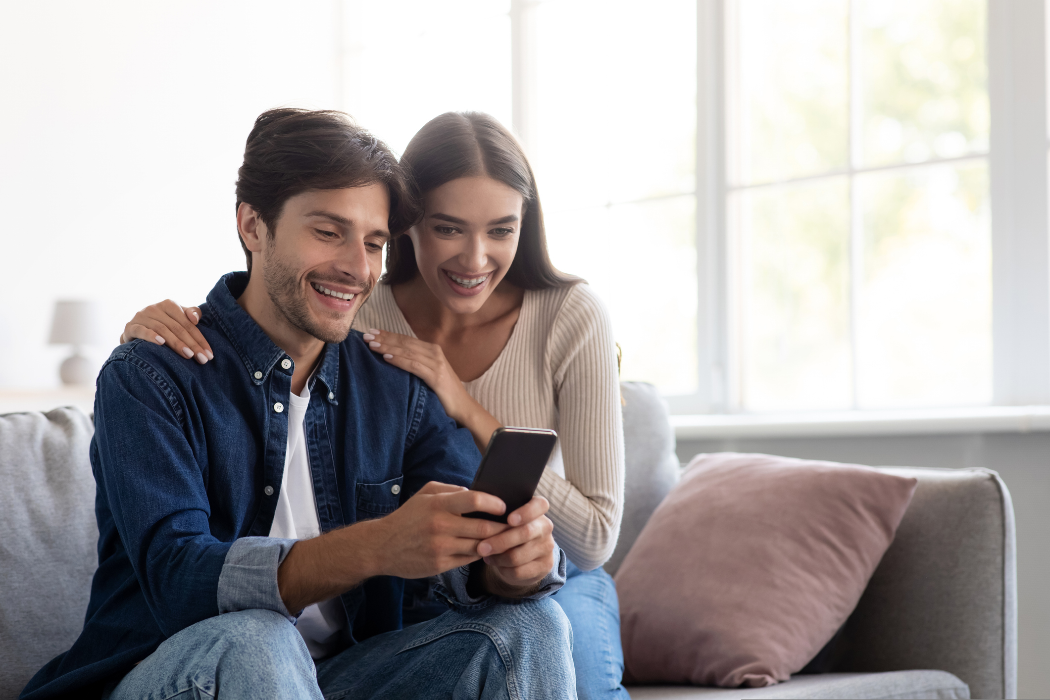 Couples smiling looking at their smart phone browsing bridging loan options