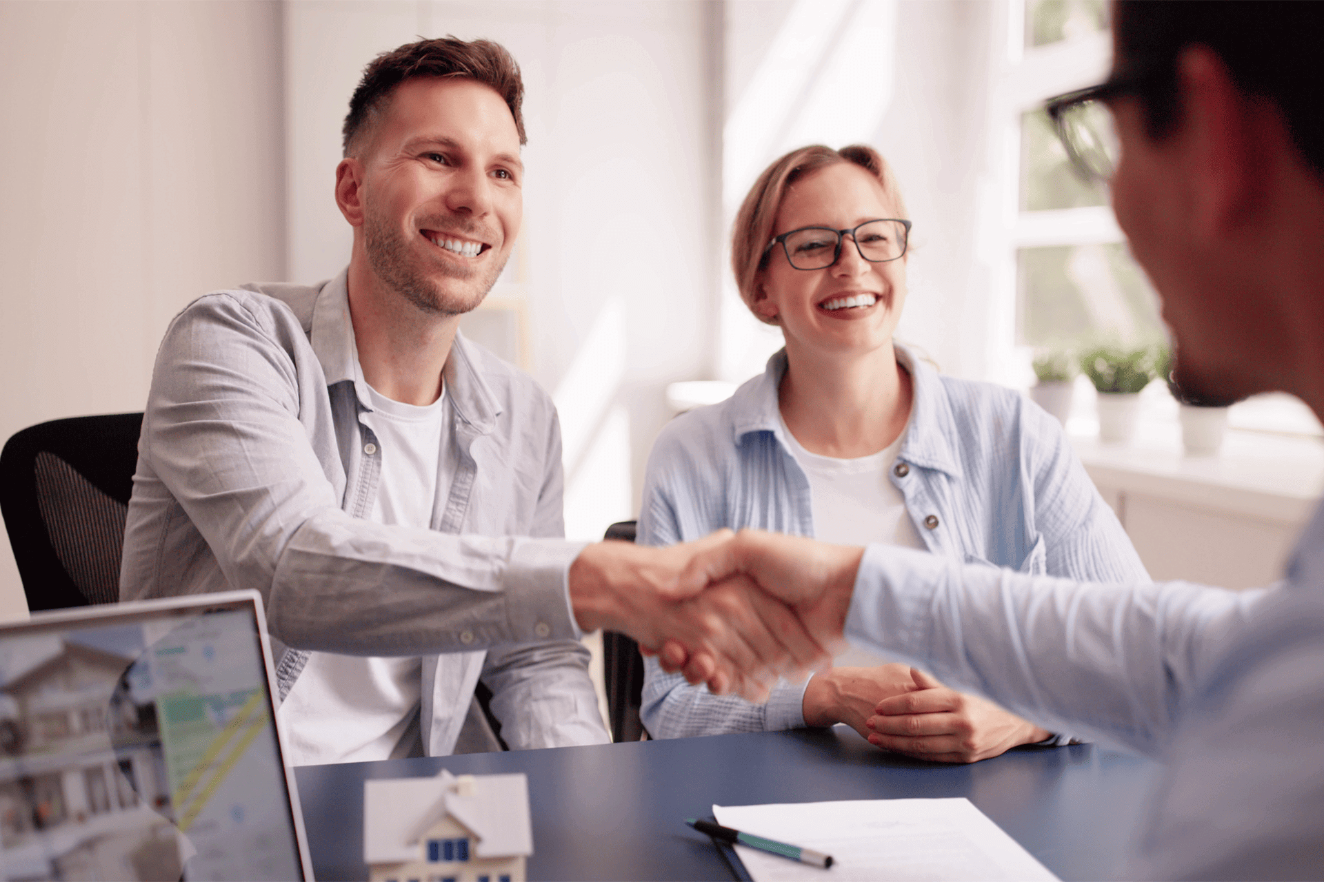 Smiling Canberra couple shaking hands with a mortgage broker during a property finance meeting, representing bridging loan and buy-before-you-sell financing.